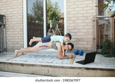 Family Sport Activity. Middle Age Caucasian Mother With Toddler Son Doing Distant Remote Online Fitness Workout On House Backyard With Laptop. Parent Exercising With Child Boy Kid. Sport At Home.