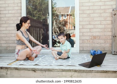 Family Sport Activity. Middle Age Caucasian Mother With Toddler Son Doing Distant Remote Online Yoga Fitness Workout On House Backyard With Laptop. Parent Exercising With Child Boy Kid. Sport At Home