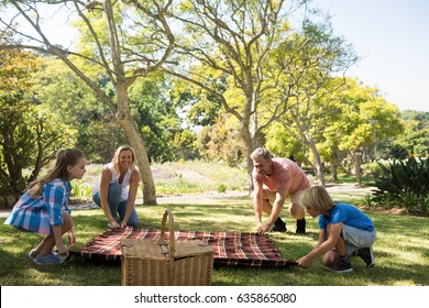 Family Spreading The Picnic Blanket In Park