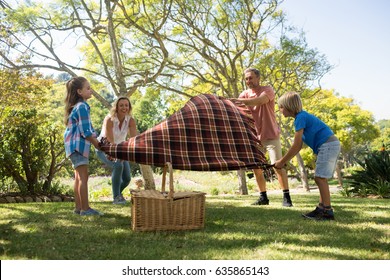 Family Spreading The Picnic Blanket In Park