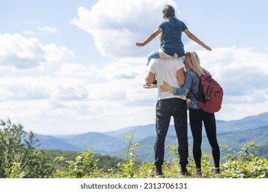 Family standing with arms around on top of mountain, looking at beautiful summer mountain landscape. People enjoying view. - Powered by Shutterstock