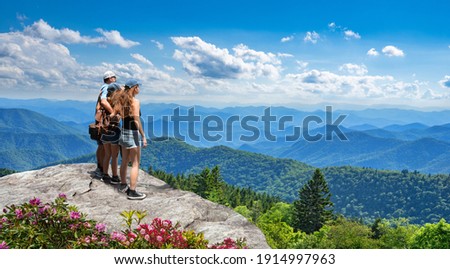 Family standing with arms around on top of mountain, looking at beautiful summer mountain landscape. People enjoying view. Smoky Mountains in background. Near Asheaville, North Carolina, USA.