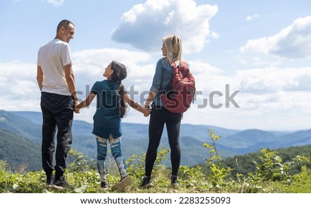 Family standing with arms around on top of mountain, looking at beautiful summer mountain landscape. People enjoying view.