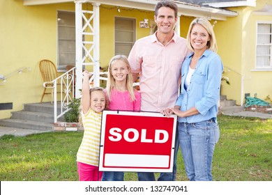 Family Standing By Sold Sign Outside Home