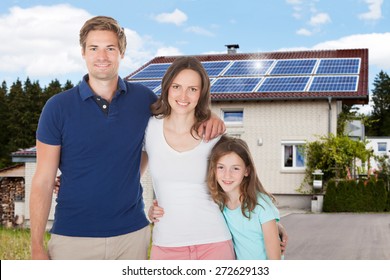 Family Standing In Front House With Solar Panel On Roof