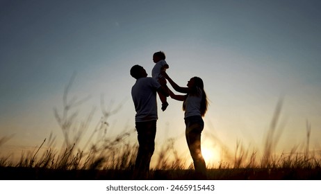 family standing on field. happy childhood concept for little child. big happy family stands on field, parents raised the child lifestyle in their arms, sunset on the background, silhouettes - Powered by Shutterstock