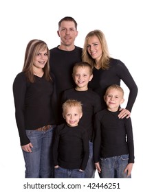 A Family Standing Together Smiling With Matching Black Shirts And Denim Pants.