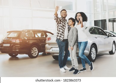 Family Stands In A Car Dealership And Takes A Selfie On The Phone. A Young Family Bought A New Car At A Large Car Dealership.