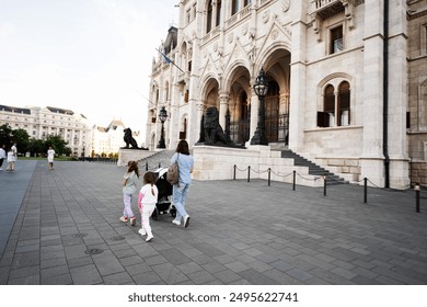 Family strolls with children and stroller near historic building on an open plaza. Urban sightseeing and family outing. - Powered by Shutterstock