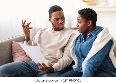 Family Struggling Financial Crisis. Confused Black Man Looking At Invoice Bills Not Able To Pay Expenses Sitting On Couch At Home. Spouses Having Finance Problems, Suffering From Coronacrisis