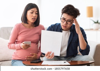 Family Struggling Financial Crisis. Depressed Japanese Couple Looking At Invoice Bills Not Able To Pay Expenses Sitting On Couch At Home. Spouses Having Finance Problems, Suffering From Coronacrisis