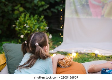 Family Summer Outdoor Movie Night. Girl Lying On Blanket And  Pillows, Eating Homemade Popcorn And Watching Film On  DIY  Screen With From Projector. Summer Outdoor Weekend Activities With Kids. 