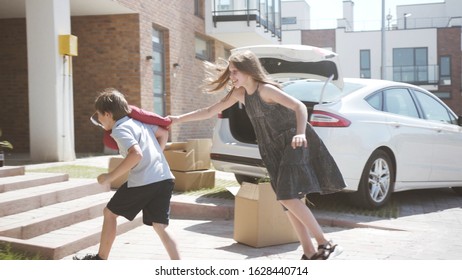 Family Summer Roadtrip To The Seaside. Two Cute Siblings Sister And Brother Loading A Heavy Suitcase In Trunk Standing Near The Car In The Courtyard.