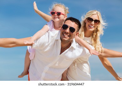 Family, Summer Vacation, Adoption And People Concept - Happy Man, Woman And Little Girl In Sunglasses Having Fun Over Blue Sky Background