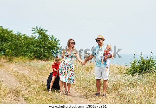 Family, summer vacation, adoption and people\
concept - happy man, woman and daughters in sunglasses, with\
suitcases having fun over blue sky\
background