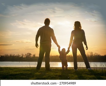 Family At Sunset Standing On The Bank Of The River