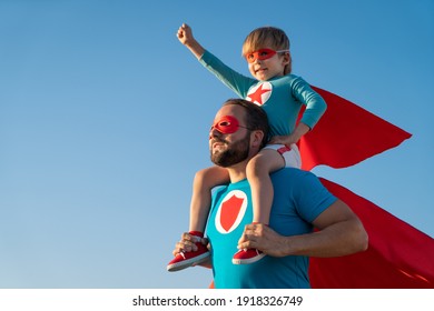 Familie der Superhelden, die sich im Freien amüsieren. Vater und Sohn, die auf blauem Sommerhintergrund spielen. Fantasie- und Freiheitskonzept