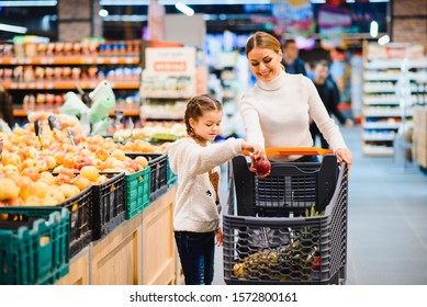 Family In The Supermarket. Beautiful Young Mom And Her Little Daughter Smiling And Buying Food. The Concept Of Healthy Eating. Harvest