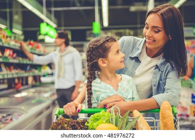 Family in the supermarket. Beautiful young mom and her little daughter are looking at each other and smiling, in the background dad is choosing goods - Powered by Shutterstock