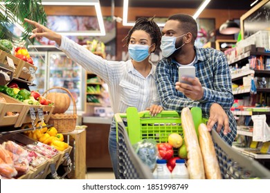 Family At Supermarket. Black Couple With Phone Doing Grocery Shopping Together Walking With Cart Full Of Food In Groceries Store, Wearing Masks. Happy Customers In Shop Concept