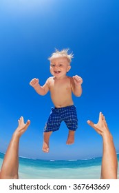 Family Swimming Fun On White Sand Sea Beach And Blue Sky - Father Hands Tossing Up Baby Boy Into Mid Air And Catching. Child Outdoor Activity, Active Lifestyle On Summer Vacation In Tropical Island.