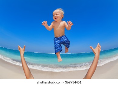 Family Swimming Fun On White Sand Sea Beach And Blue Sky - Father Hands Tossing Up Baby Boy Into Mid Air And Catching. Child Outdoor Activity, Active Lifestyle On Summer Vacation In Tropical Island.