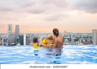 Family Swimming In Roof Top Outdoor Pool On Family Vacation In Singapore. City Skyline From Infinity Pool In Luxury Hotel. Kids Swim And Enjoy Skyscraper View In Asia. Travel With Young Children.