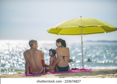 Family In Swimsuit  Having Fun At The Beach  Sitting Under A Beach Umbrella