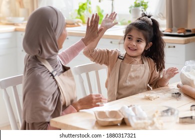 Family Teamwork. Happy Muslim Mom And Little Daughter Giving High Five To Each Other While Baking Together In Kitchen, Islamic Woman In Hijab And Her Cute Child Having Fun While Cooking Pastry