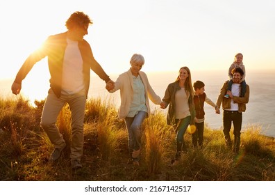 Family teamwork. A multi-generational family walking up a grassy hill together at sunset with the ocean in the background. - Powered by Shutterstock