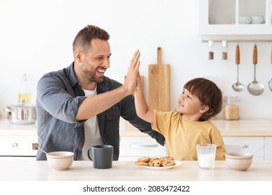 Family teamwork. Positive father and little boy giving high five and smiling to each other, enjoying healthy breakfast at kitchen, sitting together at home, free space - Powered by Shutterstock