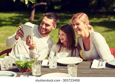 Family, Technology, Home And People Concept - Happy Family With Tablet Pc Computer Sitting And Laughing At Table In Summer Garden