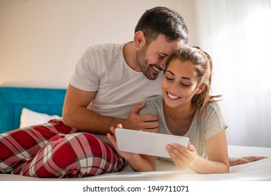 Family, technology, internet and people concept - smiling happy couple with tablet pc computer in bed at home bedroom. Close up view of beautiful smiling young wife and husband looking a tablet - Powered by Shutterstock