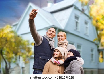 Family, Technology And Real Estate Concept - Happy Mother, Father, Daughter And Son Taking Selfie By Digital Camera Over Living House Background Outdoors In Autumn