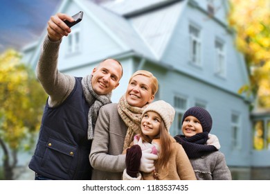 Family, Technology And Real Estate Concept - Happy Mother, Father, Daughter And Son Taking Selfie By Smartphone Over Living House Background Outdoors In Autumn