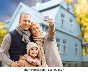 Family, Technology And Real Estate Concept - Happy Mother, Father And Daughter Taking Selfie By Smartphone Over Living House Background Outdoors In Autumn