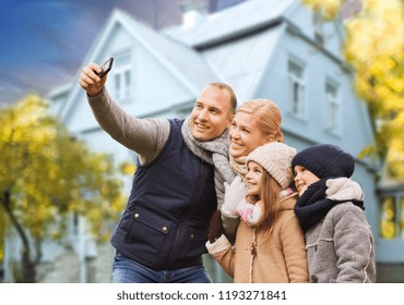 Family, Technology And Real Estate Concept - Happy Mother, Father, Daughter And Son Taking Selfie By Smartphone Over Living House Background Outdoors In Autumn