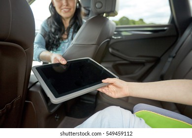 Family, Technology, Road Trip, Travel And People Concept - Happy Woman Giving Tablet Pc Computer To Her Child In Car