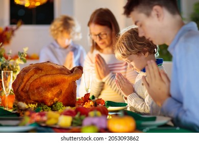 Family At Thanksgiving Dinner. Parents, Grandparents And Kids Enjoy Roasted Turkey And Vegetable Meal. Children And Grandmother Say A Thankful Prayer. Festive Home Decoration And Table Setting.