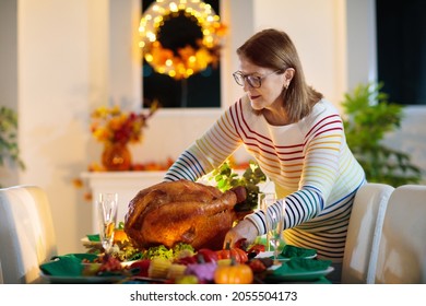 Family at Thanksgiving dinner. Parents, grandparents and kids enjoy roasted turkey and vegetable meal. Children and grandmother say a thankful prayer. Festive home decoration and table setting.