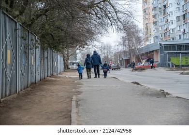 A family and their children are walking down the street. Father and mother holding hands with two children walking along the sidewalk. View from the back. Ukraine, Nikolaev - 02 05 2022.