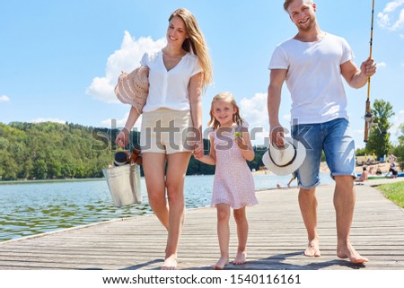 Family with their daughter on a jetty at the lake in the summer on the way to fishing