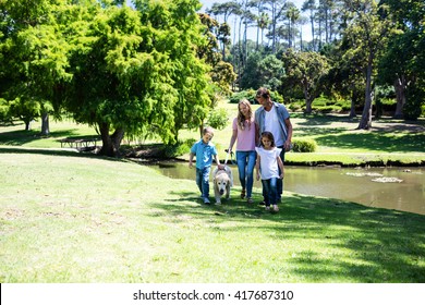 Family With Their Dog Walking In The Park Near A Pond