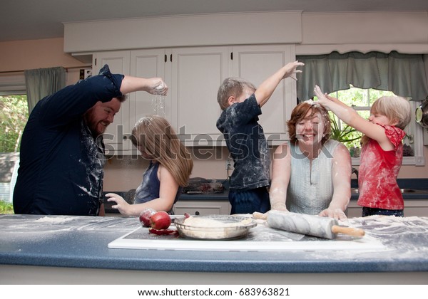 Family with three children having food fight in kitchen.
       