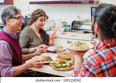 Family Of Three Are Enjoying A Dinner Together At Home. They Are Talking While Eating Homemade Curry And Salad. 