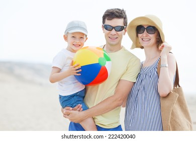 Family Of Three Enjoying Fun Day At The Beach Together Playing With The Beach Ball