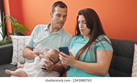 Family of three feeding baby sitting on the sofa using smartphone at home - Powered by Shutterstock