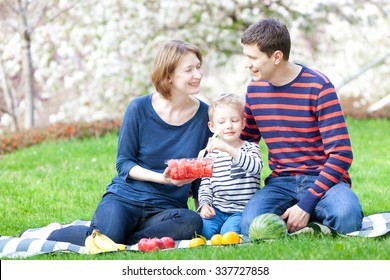 Family Of Three Having A Picnic In The Park At Spring Time