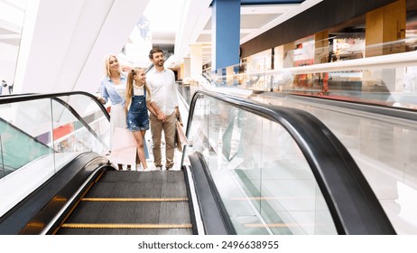 A family of three, a mother, father, and daughter, stand on a moving escalator in a brightly lit, modern shopping mall. The family is looking straight ahead as they ride the escalator up, copy space - Powered by Shutterstock