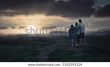 A family of three people are standing with their backs, hugging their shoulders, meeting the sunrise. A man, a woman and a child look to the future. Beautiful sunset in nature.
